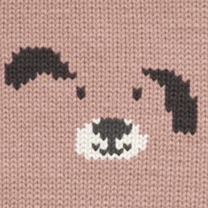 May include: Close-up of a knitted fabric with a dog face design. The dog's ears and nose are dark gray, with a white and gray muzzle. The background is a light pink color.