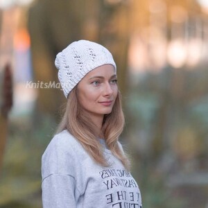 May include: A white knit beanie featuring a vertical eyelet lace pattern. The hat has a rounded crown and a textured surface with visible stitch details. The text KnitsMagic is printed in white on the left side of the beanie fabric.