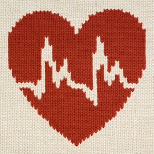 Puede incluir: Un corazón rojo tejido con una línea EKG blanca en su interior. El corazón está sobre un fondo blanco tejido.
