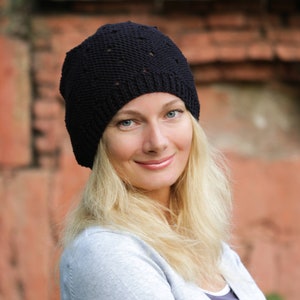 May include: A woman with long blonde hair is wearing a black knit beanie with a textured pattern. She is smiling and looking to the right of the camera.