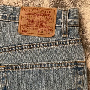 Könnte beinhalten: Hellblaue Jeans mit klassischem Fünf-Taschen-Design. Die Gesäßtasche hat ein rotes Levi's-Etikett. Das Lederetikett lautet "Levi Strauss & Co. Original Riveted Quality Clothing" mit den Maßen W 96.5 cm L 76 cm.