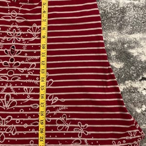 May include: Red and white striped tank top with floral and butterfly cut-out details. The top has thin straps and a scalloped hem. The length of the top is approximately 25 inches.