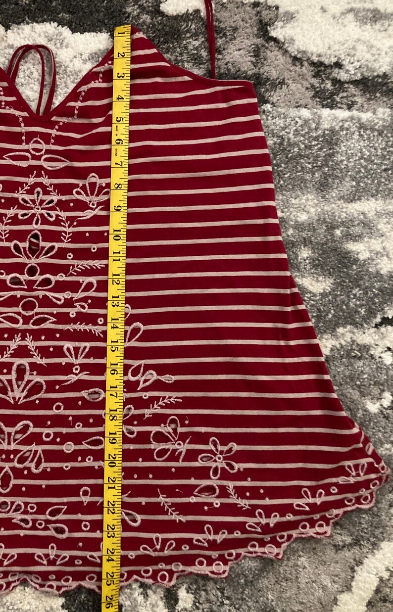 May include: Red and white striped tank top with floral and butterfly cut-out details. The top has thin straps and a scalloped hem. The length of the top is approximately 25 inches.