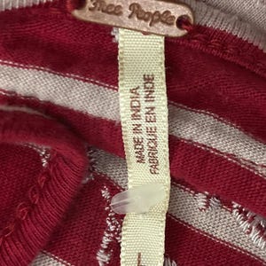 May include: Close-up of a red and white striped fabric with a tag that reads "Free People." The tag also says "Made in India" and "Fabriqu&eacute; en Inde." The size is listed as "L.G."