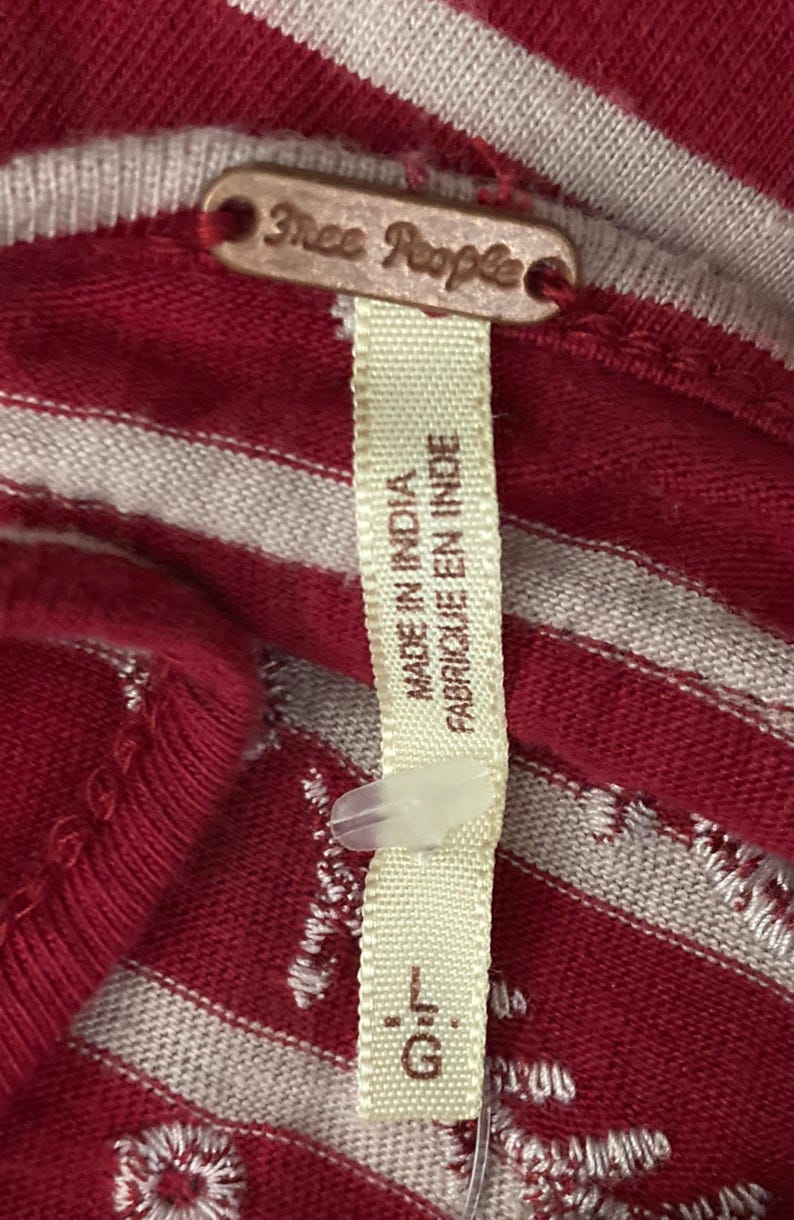 May include: Close-up of a red and white striped fabric with a tag that reads "Free People." The tag also says "Made in India" and "Fabriqu&eacute; en Inde." The size is listed as "L.G."