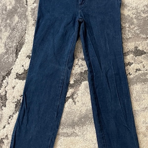 May include: Dark blue denim jeans with a classic five-pocket design. The jeans have a straight leg cut and a button and zipper closure. The fabric appears to be a medium weight denim.