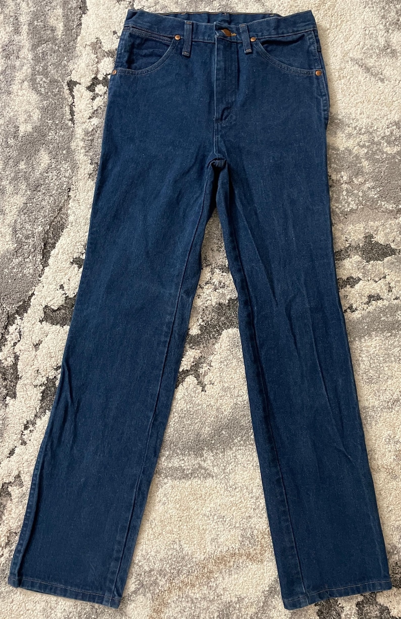 May include: Dark blue denim jeans with a classic five-pocket design. The jeans have a straight leg cut and a button and zipper closure. The fabric appears to be a medium weight denim.