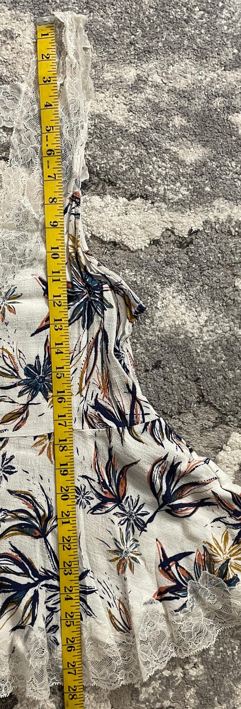 Puede incluir: Top blanco con estampado floral y ribete de encaje, medido con una cinta m&eacute;trica amarilla. La parte superior presenta un dise&ntilde;o bot&aacute;nico con acentos azul marino, naranja y marr&oacute;n. La parte superior mide aproximadamente 71 cm de largo.