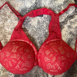 May include: A red lace bra with adjustable straps and a hook-and-eye closure. The bra features a floral lace pattern over a nude lining, creating a contrast. The bra is designed for support and style.