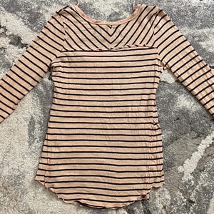 May include: A long-sleeved, striped shirt in a light pink color with dark brown stripes. The shirt has a scoop neck and a unique lace detail on the sleeves.