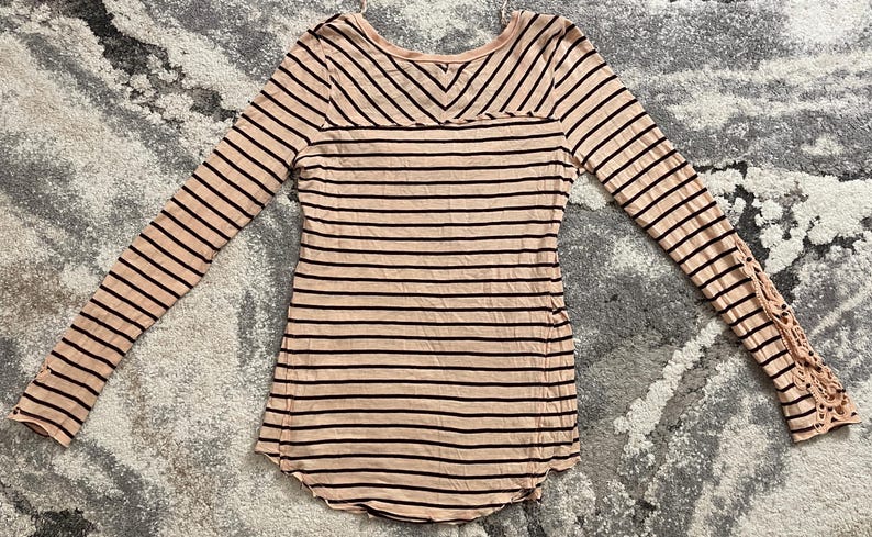 May include: A long-sleeved, striped shirt in a light pink color with dark brown stripes. The shirt has a scoop neck and a unique lace detail on the sleeves.