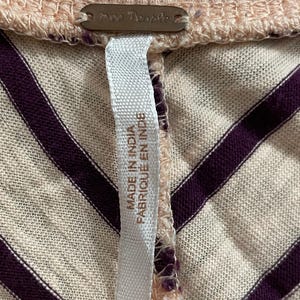 May include: Close-up of a light pink and cream-colored top with dark purple diagonal stripes. The top has a ribbed neckline and a tag that reads "Free People" and "Made in India / Fabriqu&eacute; en Inde".