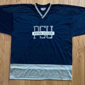 Könnte beinhalten: Marineblaues Hockey-Trikot mit grauen Akzenten an Ärmeln und Saum. Das Trikot trägt den Text "PSU" über "PENN STATE" in einem weißen Rechteck. Das Trikot hat einen V-Ausschnitt.
