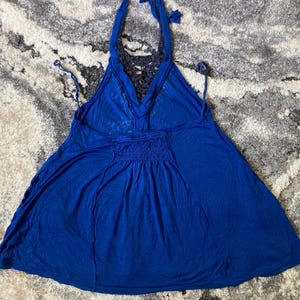 K&ouml;nnte beinhalten: Ein leuchtend blaues Neckholder-Top mit flie&szlig;ender Silhouette. Das Top hat einen geh&auml;kelten R&uuml;ckenteil und ein gerafftes Detail an der Taille. Die Neckholder-Tr&auml;ger werden im Nacken gebunden.