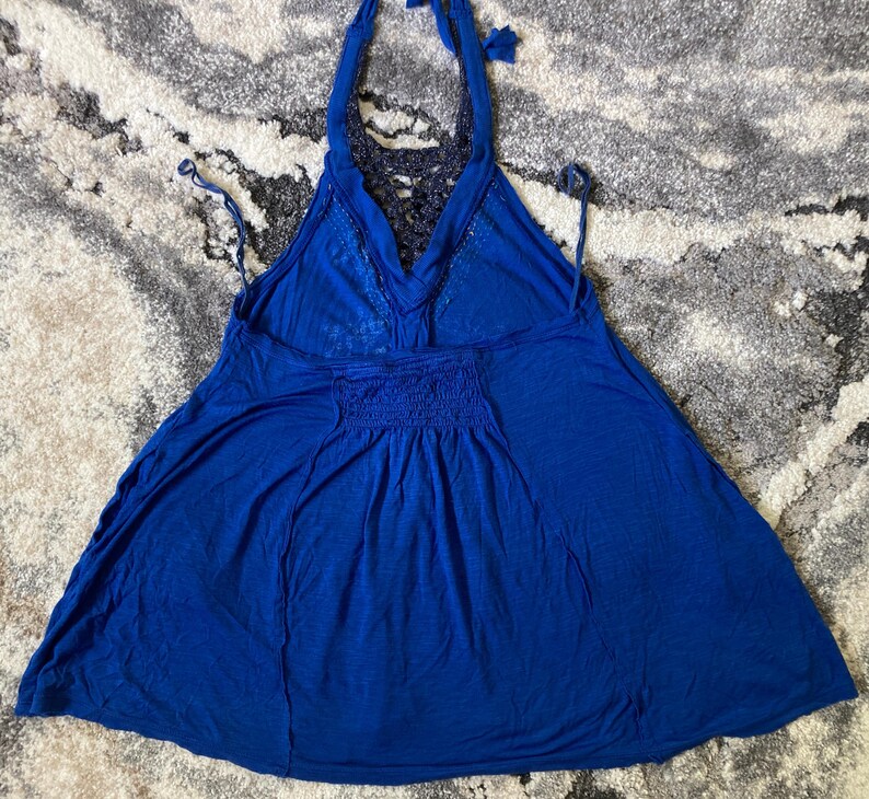 K&ouml;nnte beinhalten: Ein leuchtend blaues Neckholder-Top mit flie&szlig;ender Silhouette. Das Top hat einen geh&auml;kelten R&uuml;ckenteil und ein gerafftes Detail an der Taille. Die Neckholder-Tr&auml;ger werden im Nacken gebunden.