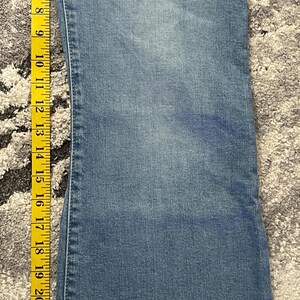 Puede incluir: Vaqueros de mezclilla azul claro con pernera acampanada, medidos con una cinta m&eacute;trica amarilla. Los vaqueros miden aproximadamente 73,66 cm de largo, con costuras y dobladillos visibles. La tela tiene un aspecto descolorido.