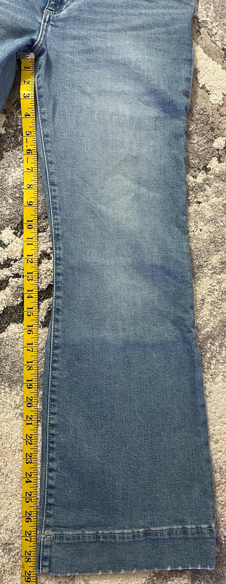 Puede incluir: Vaqueros de mezclilla azul claro con pernera acampanada, medidos con una cinta m&eacute;trica amarilla. Los vaqueros miden aproximadamente 73,66 cm de largo, con costuras y dobladillos visibles. La tela tiene un aspecto descolorido.