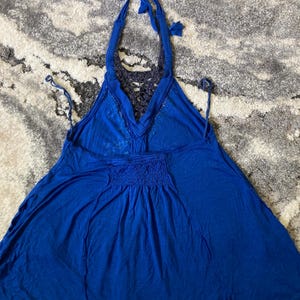 K&ouml;nnte beinhalten: Ein leuchtend blaues Neckholder-Top mit einzigartigem Design. Das Top hat einen Neckholder-Ausschnitt mit Bindeb&auml;ndern, einen detaillierten R&uuml;cken und eine geraffte Taille. Der Stoff wirkt leicht und flie&szlig;end, perfekt f&uuml;r warmes Wetter.