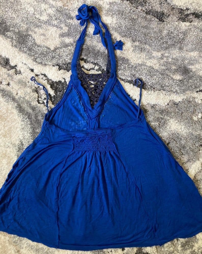 K&ouml;nnte beinhalten: Ein leuchtend blaues Neckholder-Top mit einzigartigem Design. Das Top hat einen Neckholder-Ausschnitt mit Bindeb&auml;ndern, einen detaillierten R&uuml;cken und eine geraffte Taille. Der Stoff wirkt leicht und flie&szlig;end, perfekt f&uuml;r warmes Wetter.