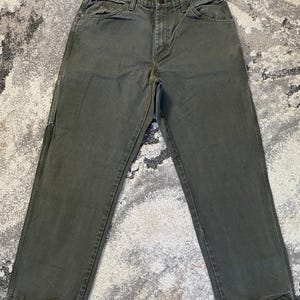 Puede incluir: Pantalones de trabajo de color verde oliva con un diseño clásico de cinco bolsillos, cierre de botones y costuras reforzadas a lo largo de las perneras. Estos pantalones resistentes tienen un corte recto con cintura estructurada y trabillas.
