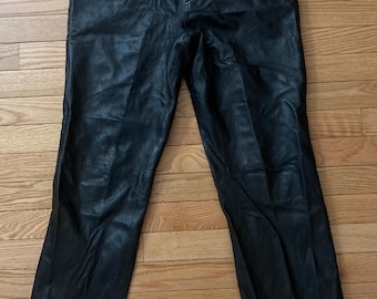 May include: Black leather pants with a classic five-pocket design. The pants have a button and zipper closure and are made of a smooth, shiny leather material. The pants are laid flat on a wooden surface.