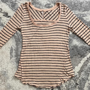 May include: A long-sleeved, scoop-neck shirt with horizontal black stripes on a light pink background. The sleeves have a lace detail at the wrist. The shirt is made of a soft, lightweight material.