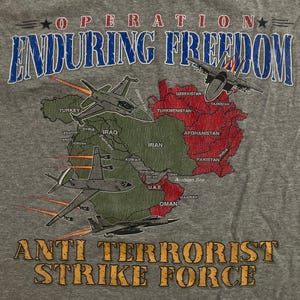 May include: Gray t-shirt with the text "OPERATION ENDURING FREEDOM" and "ANTI TERRORIST STRIKE FORCE." The shirt features a map of the Middle East with military jets flying over it.