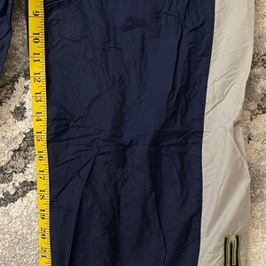 Pu&ograve; includere: Pantaloni sportivi blu navy e grigi con il logo Nike in verde. I pantaloni sono lunghi circa 76 cm, misurati con un metro a nastro giallo.