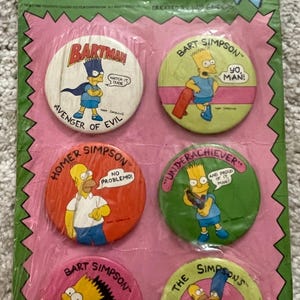May include: A vintage button collection featuring The Simpsons characters. The buttons showcase Bart, Homer, and other characters with phrases like "No Problemo!" and "Yo, Man!" The buttons are in a pink and green package.