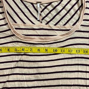 May include: A cream-colored, scoop-neck shirt with dark burgundy horizontal stripes. The shirt is measured with a yellow tape measure, showing a width of approximately 17 inches.