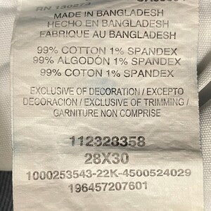 Puede incluir: Una etiqueta blanca con texto que indica el origen, la composici&oacute;n y la talla de la prenda. La etiqueta dice "HECHO EN BANGLADESH" y la talla es "28X30". La tela es 99% algod&oacute;n y 1% elastano.
