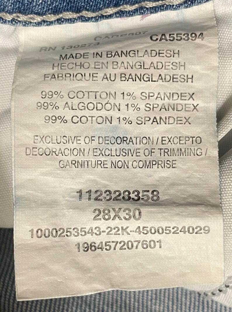 Puede incluir: Una etiqueta blanca con texto que indica el origen, la composici&oacute;n y la talla de la prenda. La etiqueta dice "HECHO EN BANGLADESH" y la talla es "28X30". La tela es 99% algod&oacute;n y 1% elastano.