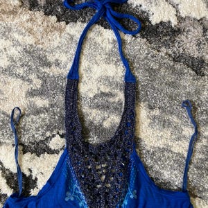 K&ouml;nnte beinhalten: Ein blaues Neckholder-Top mit geh&auml;keltem Ausschnitt und Kordelverschluss. Das Top hat ein detailliertes H&auml;keldesign in einem dunkleren Blauton mit einem helleren blauen Stickmuster auf der Vorderseite.