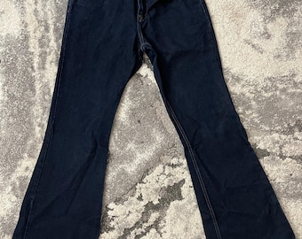 May include: Dark wash denim jeans with a flared leg. The jeans have a classic five-pocket design, a button and zipper closure, and belt loops. The stitching is a contrasting light brown color.