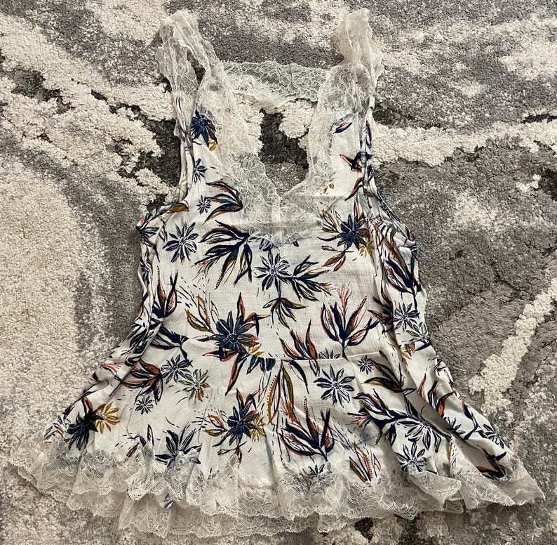 Puede incluir: Camiseta sin mangas blanca con estampado floral con ribete y espalda de encaje. La camiseta sin mangas presenta un escote en V y un estampado floral en azul marino, marr&oacute;n y naranja. El ribete de encaje es blanco.