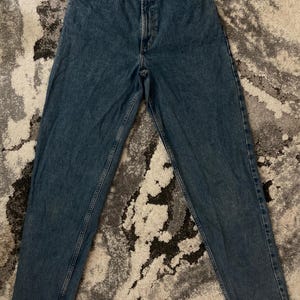 Puede incluir: Un par de vaqueros de mezclilla azul vintage con cintura alta y corte relajado. Los vaqueros tienen un diseño clásico de cinco bolsillos, cierre de botón y cremallera, y la marca "GAP" es visible en la cintura.