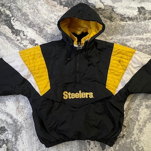 以下が含まれることがあります： 黒と黄色のフード付きジャケット。金色の文字で「Steelers」と書かれています。 ジャケットは黒色のボディで、袖と肩に黄色と白のアクセントがあります。 フードは黄色い裏地です。