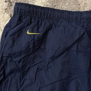 Pu&ograve; includere: Pantaloni sportivi blu navy con elastico in vita e tasca laterale. Un logo Nike swoosh giallo &egrave; visibile sulla parte superiore sinistra dei pantaloni. I pantaloni sono realizzati in materiale leggero, possibilmente nylon.