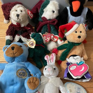 May include: A collection of plush toys, including teddy bears, a penguin, and a rabbit. The toys are in various colors, with some wearing hats and scarves. Some toys have tags attached.
