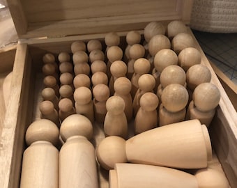 May include: A wooden box filled with various sizes of wooden peg dolls. The dolls are all natural wood color and have a smooth finish.