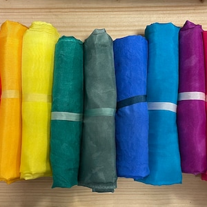 May include: Ten rolls of fabric in various colors, including red, orange, yellow, green, blue, purple, and pink. The fabric is rolled up and tied with a ribbon.