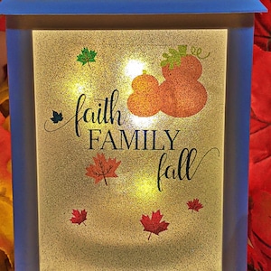 May include: White lantern with a frosted glass panel featuring the text "faith family fall" with a pumpkin design and fall leaves.