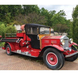 May include: A vintage red fire truck with black canvas top and wooden accents. The truck has a large hose and a sign that reads "Monterey Fire Dept."