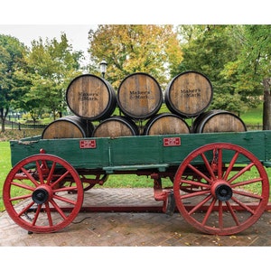May include: A green wooden wagon with red wheels, carrying six wooden barrels. The barrels are stacked in two rows of three, and each barrel is labeled "Maker's Mark".