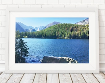 May include: A framed photograph of a mountain lake with a forest in the background. The lake is a bright blue and the forest is a lush green. The mountains are in the distance and are covered in trees.