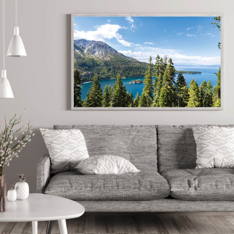 May include: A framed photograph of a scenic landscape with a lake surrounded by mountains and trees. The lake is a bright blue color and the mountains are covered in green trees. The sky is a light blue with white clouds.
