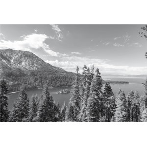 May include: A black and white photograph of a mountain lake with a small island in the middle. The lake is surrounded by trees and mountains. The sky is cloudy.