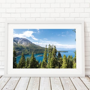 May include: A framed photograph of a scenic view of a lake surrounded by mountains and trees. The lake is a bright blue color and the mountains are covered in trees and snow. The sky is a clear blue with white clouds.