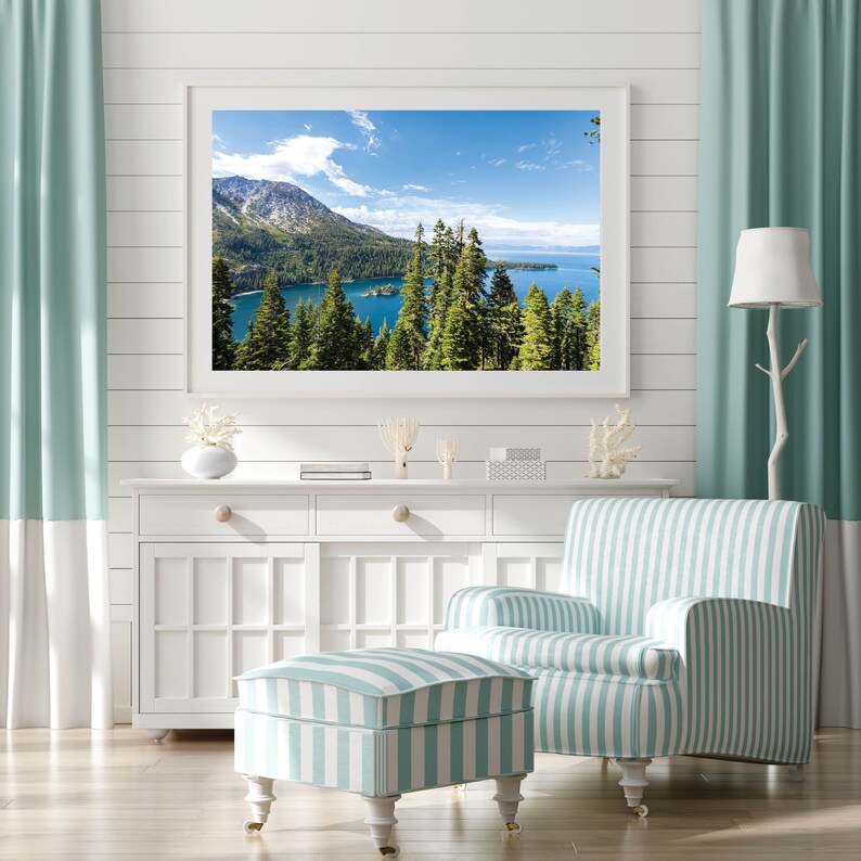 May include: A framed photograph of a lake surrounded by trees and mountains. The lake is a bright blue color and the mountains are covered in snow. The sky is a light blue with white clouds.