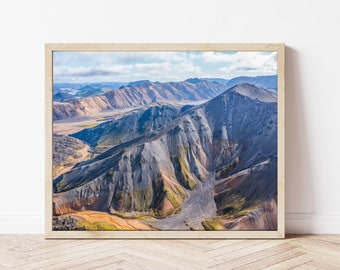 May include: An aerial view of a mountain range with a valley in the center. The mountains are a mix of gray, brown, and green, with a hint of blue in the distance. The valley is filled with a mix of gray and brown rocks.